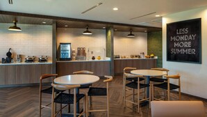 A modern cafe with wooden flooring, round tables, and black chairs. There is a counter with various items and a sign on the wall that reads "LESS MONDAY MORE SUMMER". - Fairfield By Marriott Inn & Suites Foley (Foley)