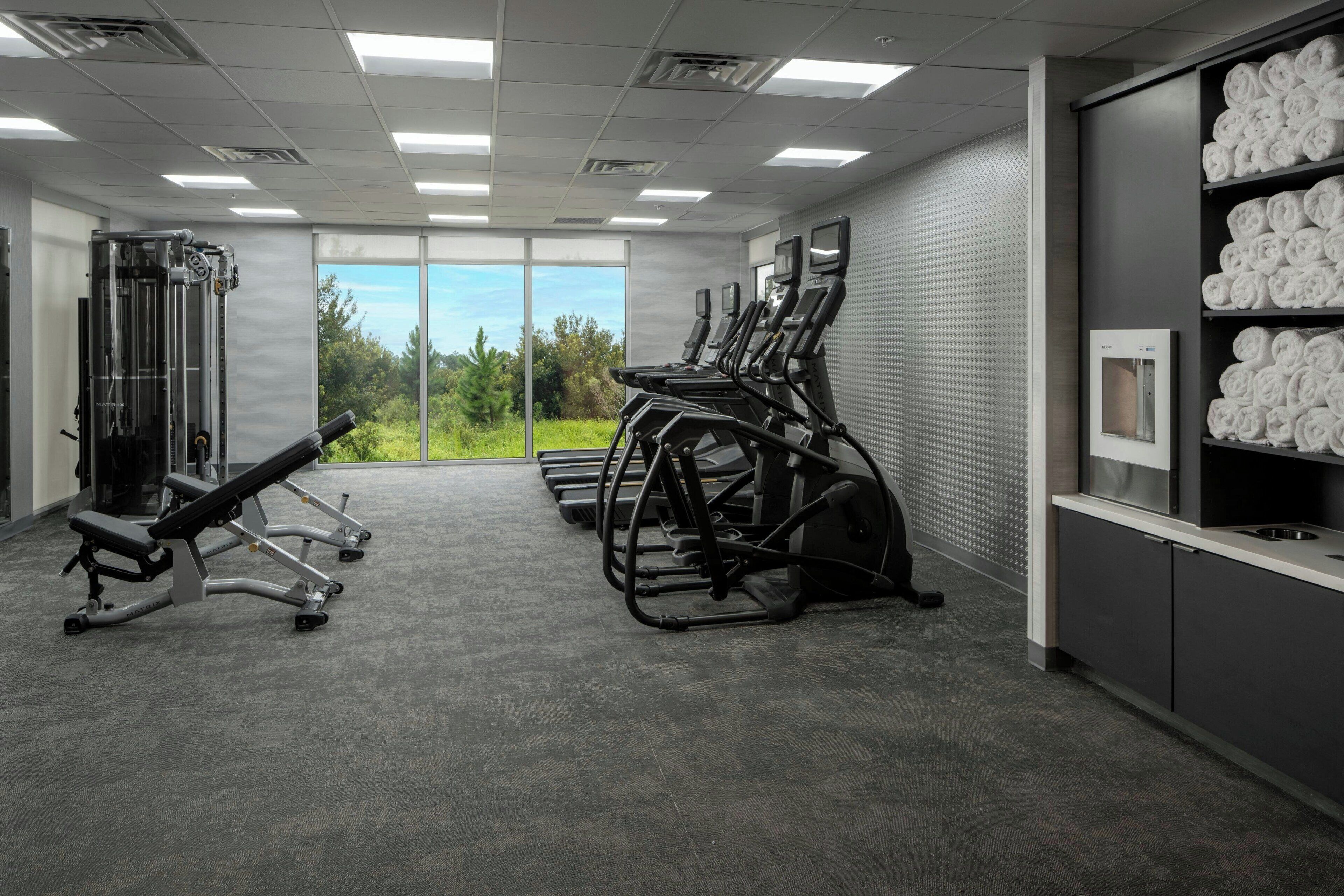 A gym with exercise equipment, a large window with a view of greenery, and a towel rack.