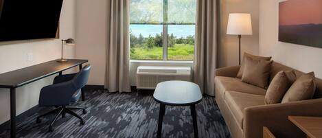 A hotel room with a desk, office chair, sofa, and a window with a view of greenery.