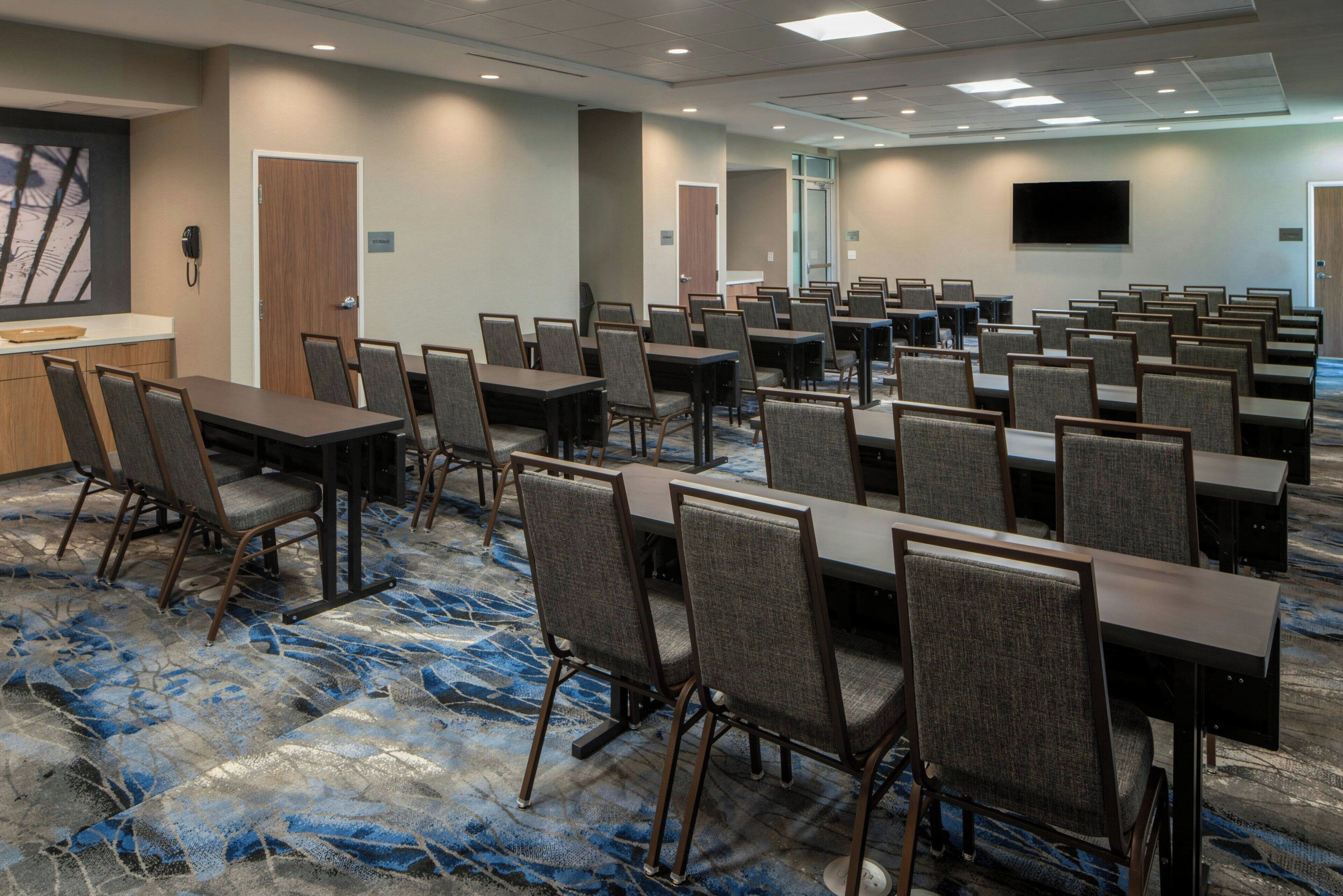 A conference room with multiple tables and chairs, a large screen, and a carpeted floor.
