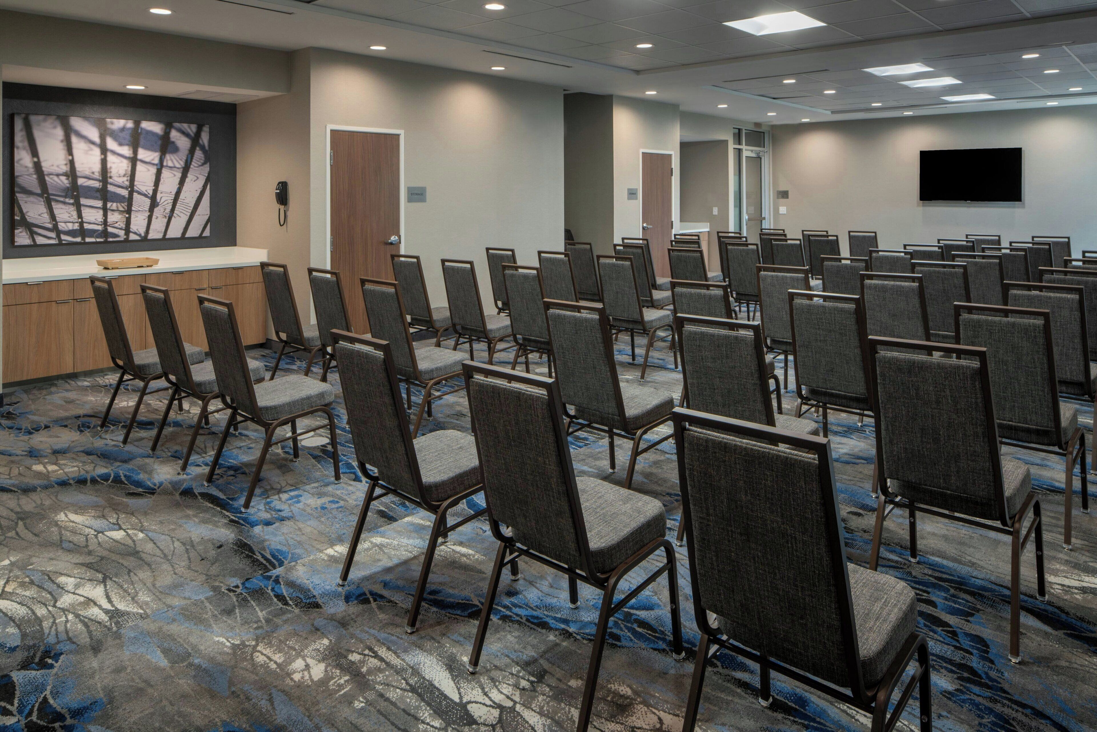 A conference room with rows of chairs, a reception desk, a phone, and a TV on the wall.