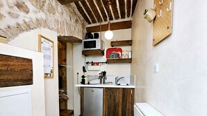 A narrow kitchen with wooden beams, a hanging light, and a pegboard with hooks.