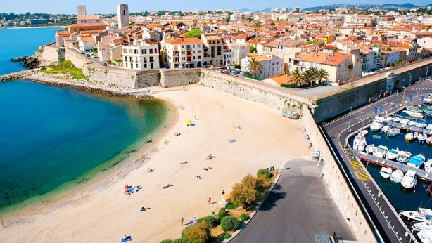 Eine Küstenstadt mit Sandstrand, einer Steinmauer und einem Jachthafen mit Booten.