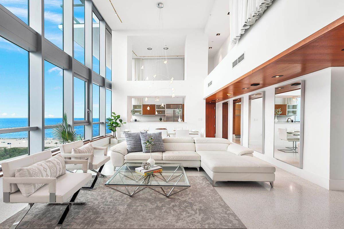 A spacious living area with large windows overlooking a beach, a modern kitchen, and a dining area.