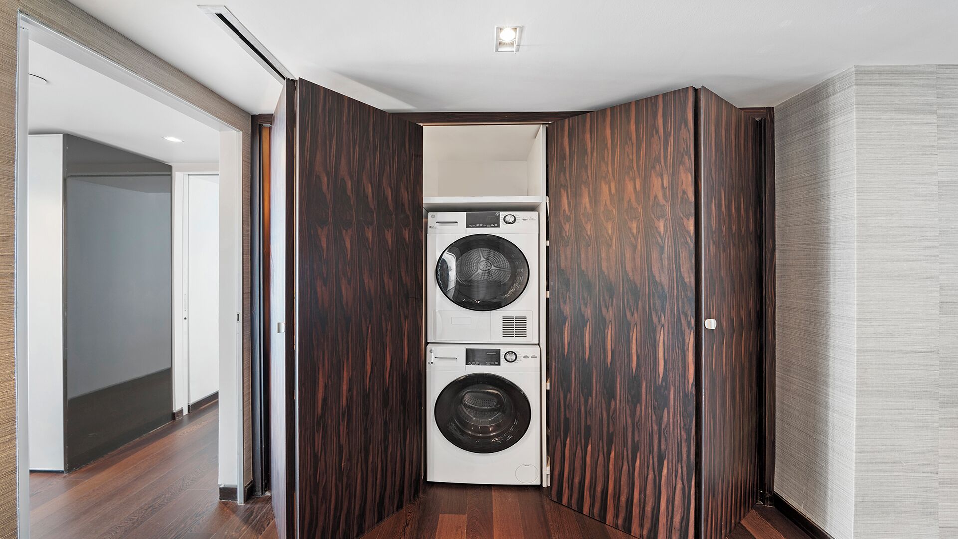 A laundry room with two stacked washing machines, wooden paneling on the walls, and a wooden floor.
