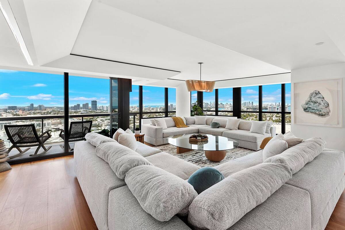 A spacious living room with a large sectional sofa, a coffee table, and a city view through large windows.