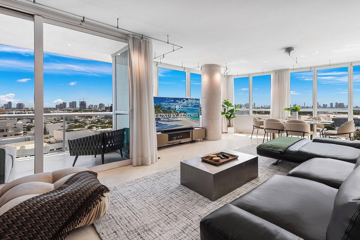 A spacious living room with a large window, a flat-screen TV, a sofa, a coffee table, and a dining area with chairs.