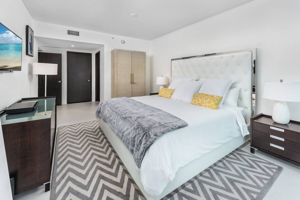 A modern hotel room with a large bed, a desk, and a wardrobe.