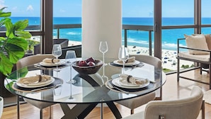 Uma sala de jantar com mesa de vidro, quatro cadeiras e vista para a praia.