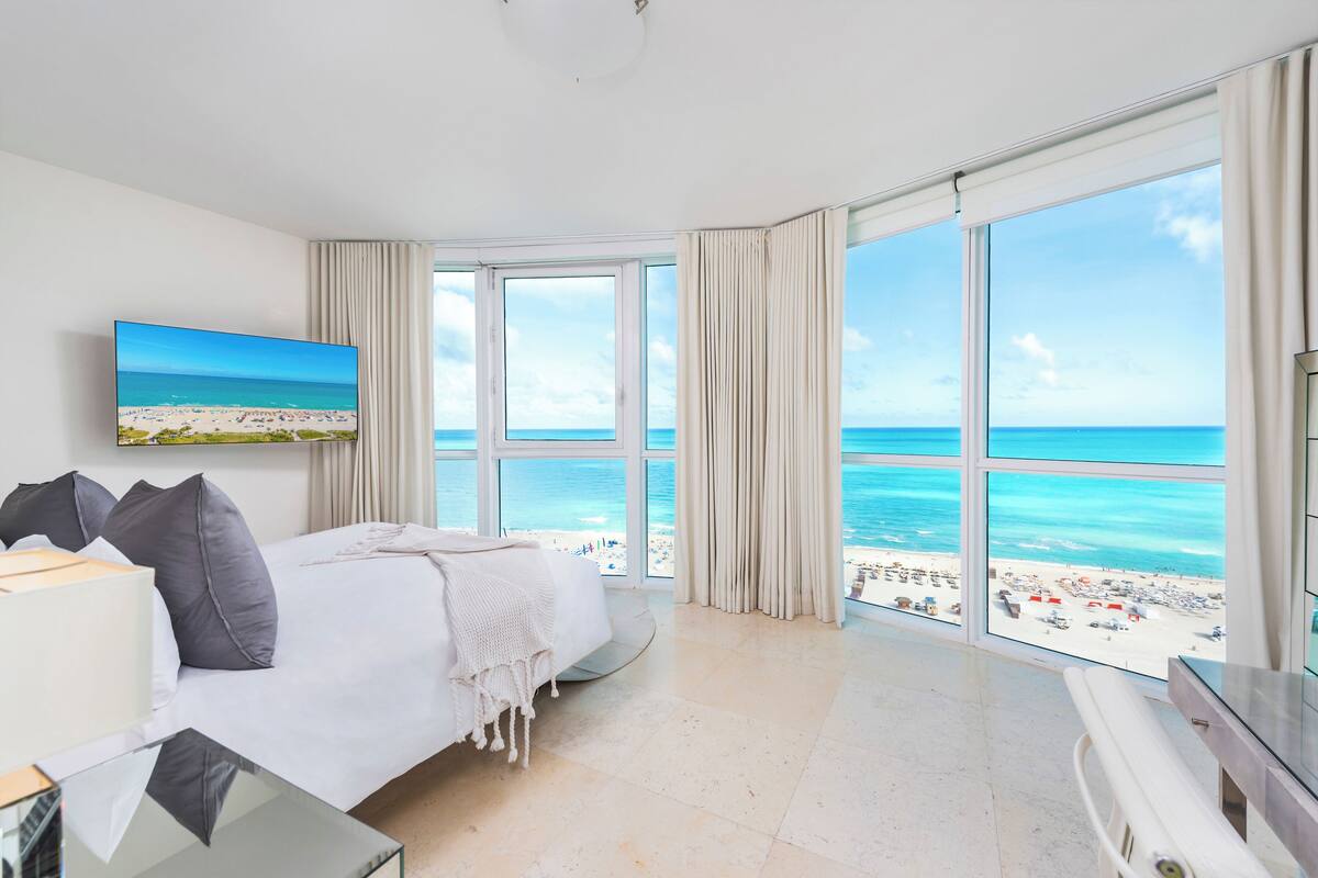 A hotel room with a large bed, a TV, and a view of the beach.