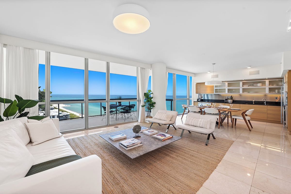 A spacious living room with a large window overlooking the sea, a dining area with a view, and a modern kitchen.