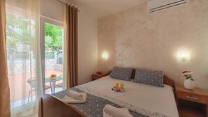 A hotel room with a bed, bedside tables, a small table with fruit, and a view of the outside. - Villa Sunny Hill (Budva)