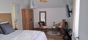 A bedroom with a bed, a wooden wardrobe, a mirror, wicker chairs, a small table with items, and a TV mounted on the wall. - Suite for 4 people, 2 bedrooms, 2 bathrooms - Baie Mont St. Michel (Le Val-Saint-Père)