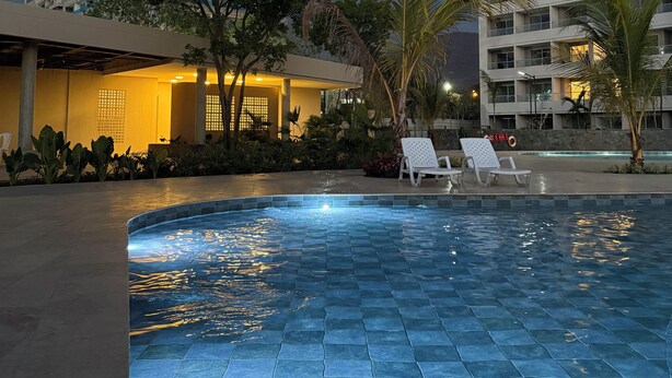 A swimming pool with tiled flooring, surrounded by lounge chairs and palm trees.