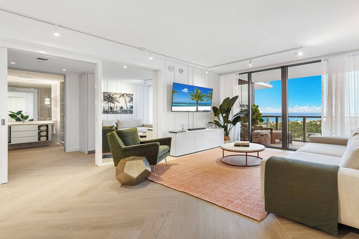 A modern living room with a large window offering a view of the sea, a sofa, a coffee table, and a green armchair.