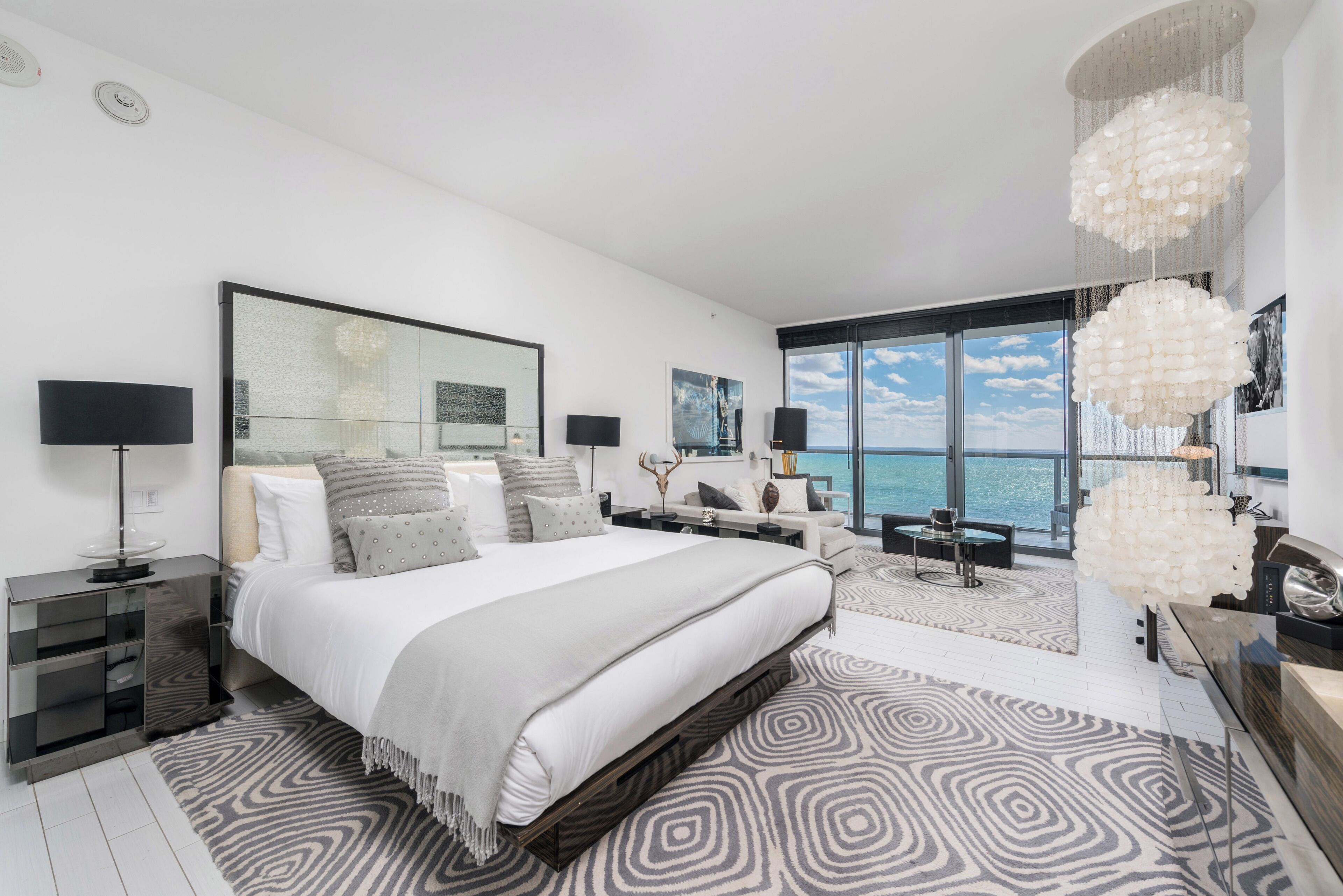 A modern bedroom with a large bed, a view of the ocean, and a chandelier.