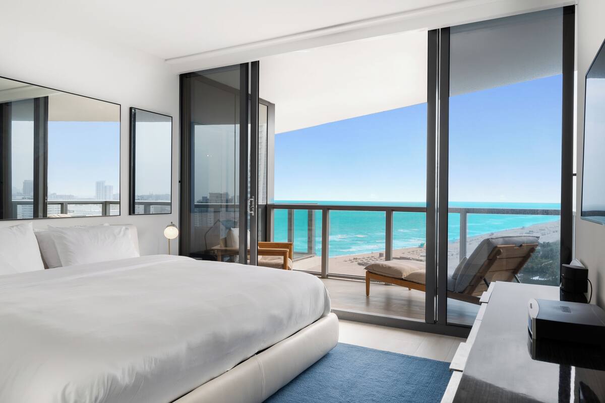 A modern hotel room with a large bed, a desk, and a view of the ocean.