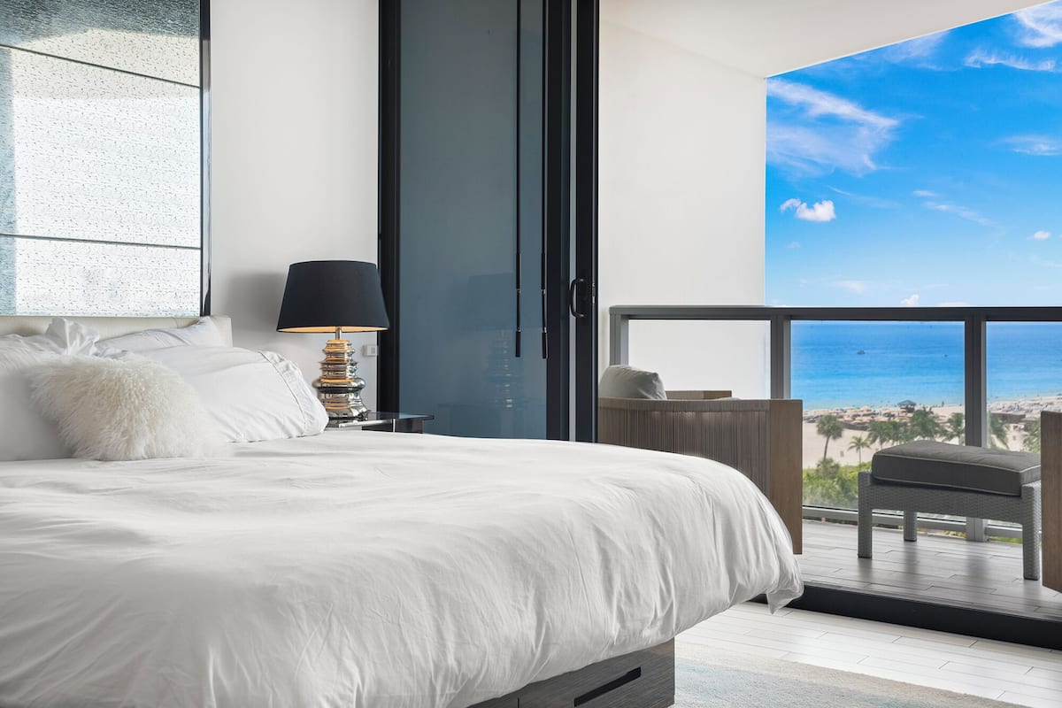 A bedroom with a large bed, a bedside lamp, and a view of the ocean through a balcony.