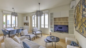 A modern living room with a sofa, chairs, a dining table, and a TV. - L'instant Bassin - Air Conditionné et proche plage d'Arcachon (Arcachon)