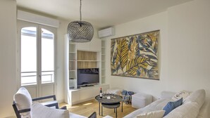 A modern living room with a sofa, chairs, a coffee table, and a TV. There is a large artwork on the wall and a hanging light fixture. - L'instant Bassin - Air Conditionné et proche plage d'Arcachon (Arcachon)