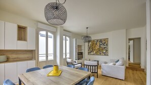 A modern living room with a wooden dining table, blue chairs, a white sofa, and a large abstract painting on the wall. - L'instant Bassin - Air Conditionné et proche plage d'Arcachon (Arcachon)