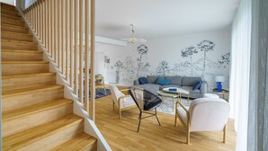 A modern living room with a wooden staircase, a grey sofa, and a patterned wall. - Ti Armor - Maison à 200m de la plage (Benodet)