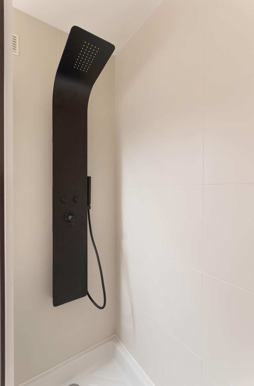 A modern shower with a curved design, mounted on a wall with white tiles.