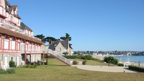 Un bâtiment situé sur la côte, avec une façade rouge, un escalier menant à un balcon et une vue sur la mer.