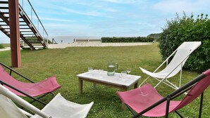 Un espace extérieur verdoyant avec une table dressée pour deux personnes, deux chaises et un escalier menant à la plage.