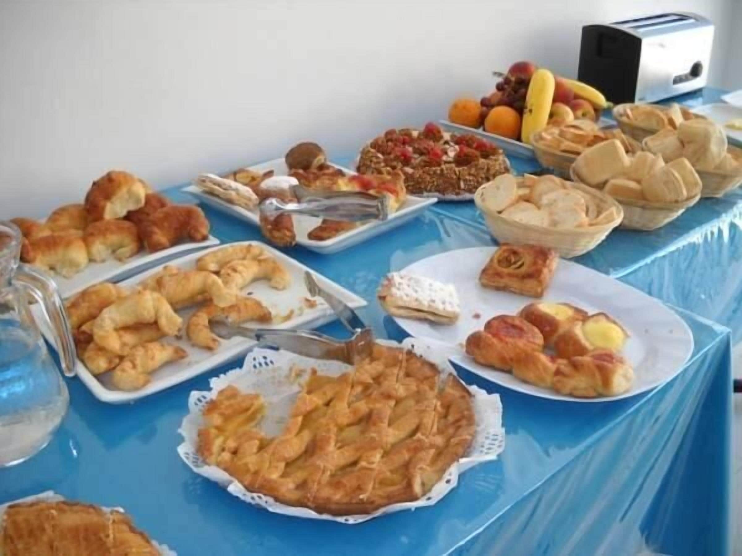 A table with various pastries and fruits, a toaster, and a glass pitcher.