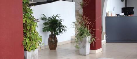 A spacious lobby with a modern design, featuring a reception desk, potted plants, and a tiled floor.