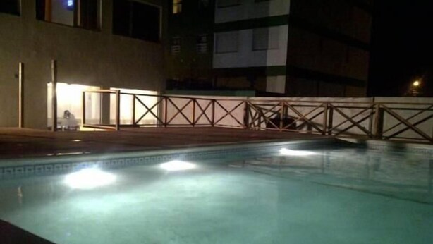 A swimming pool at night with a fence and a building in the background. - Terra do Mar (San Bernardo del Tuyú)