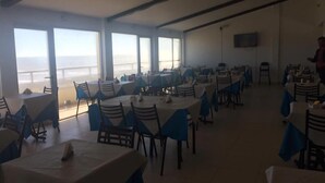 A dining area with tables and chairs, large windows, and a view of the sea. - Terra do Mar (San Bernardo del Tuyú)