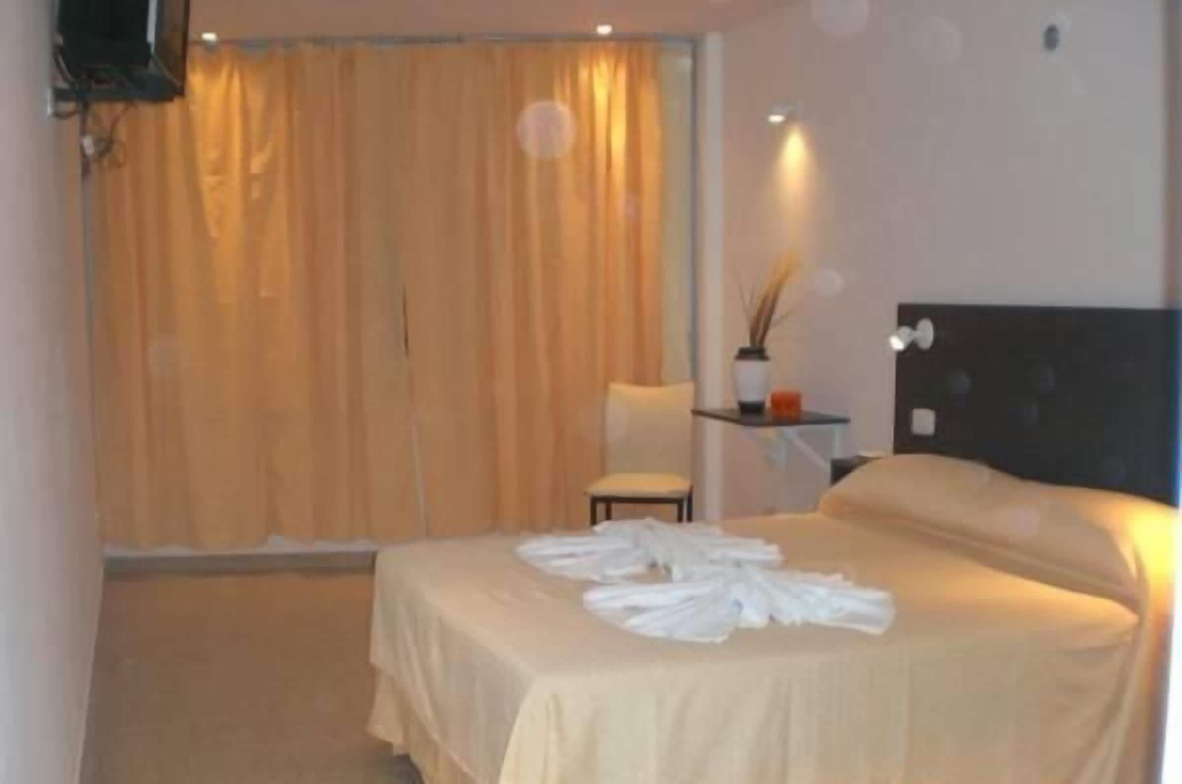 A hotel room with a bed, a chair, a small table, and a curtain.