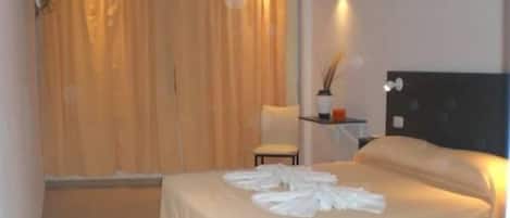 A hotel room with a bed, a chair, a small table, and a curtain.