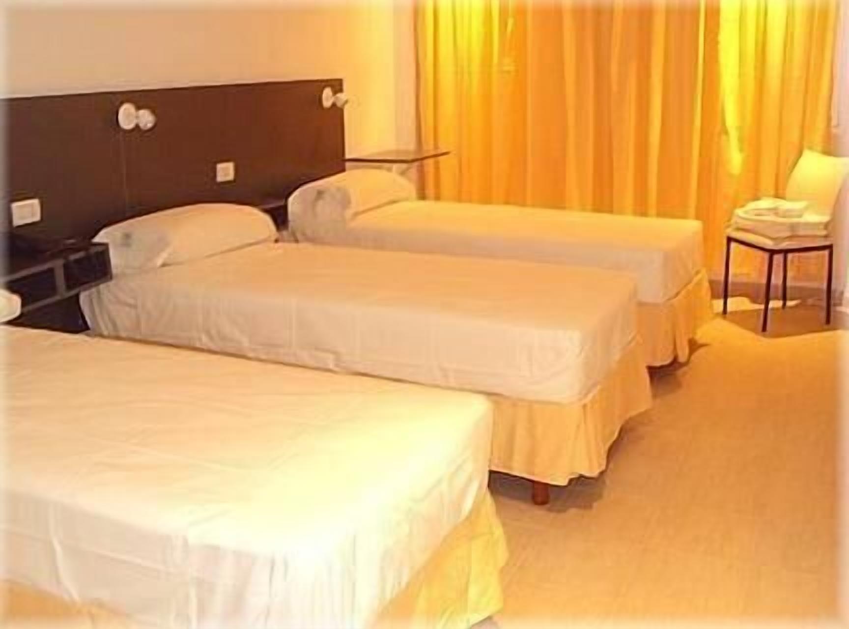 Una habitación de hotel con dos camas individuales, una mesita de noche, una silla y una cortina.
