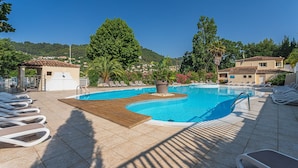 A swimming pool with sun loungers, a wooden deck, and a view of a hillside with buildings.