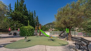 A playground with green artificial turf, a slide, and a climbing structure.