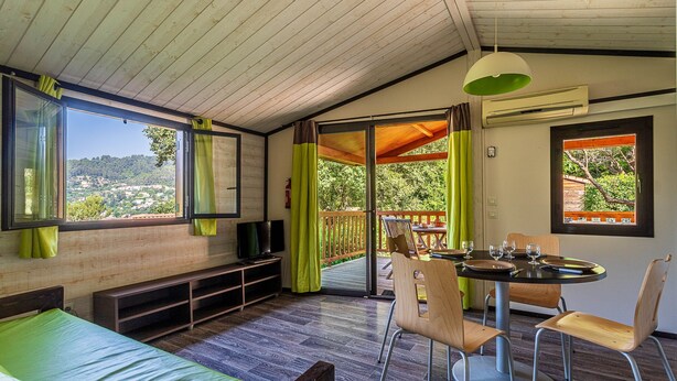 A room with a bed, a table with chairs, a television, and a view of the outdoors.