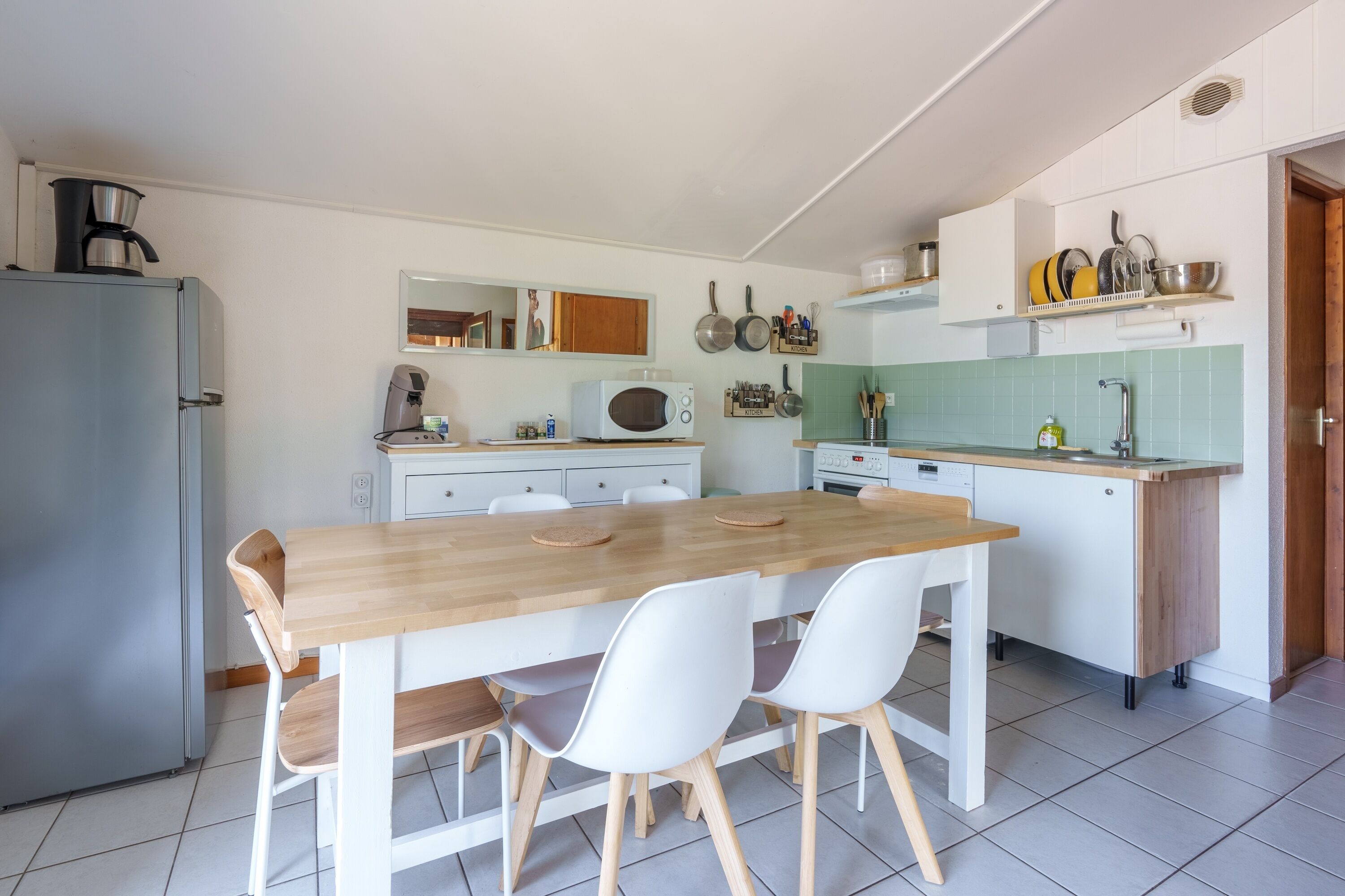 A compact kitchen with a wooden dining table, white chairs, a refrigerator, a microwave, and a sink.