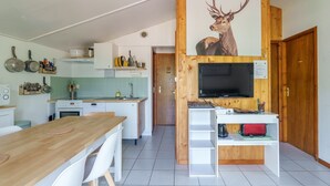 A modern kitchen with a wooden dining table, white chairs, a built-in TV, and a mounted deer artwork. - Chalet des cimes - Avec jardin (La Bresse)