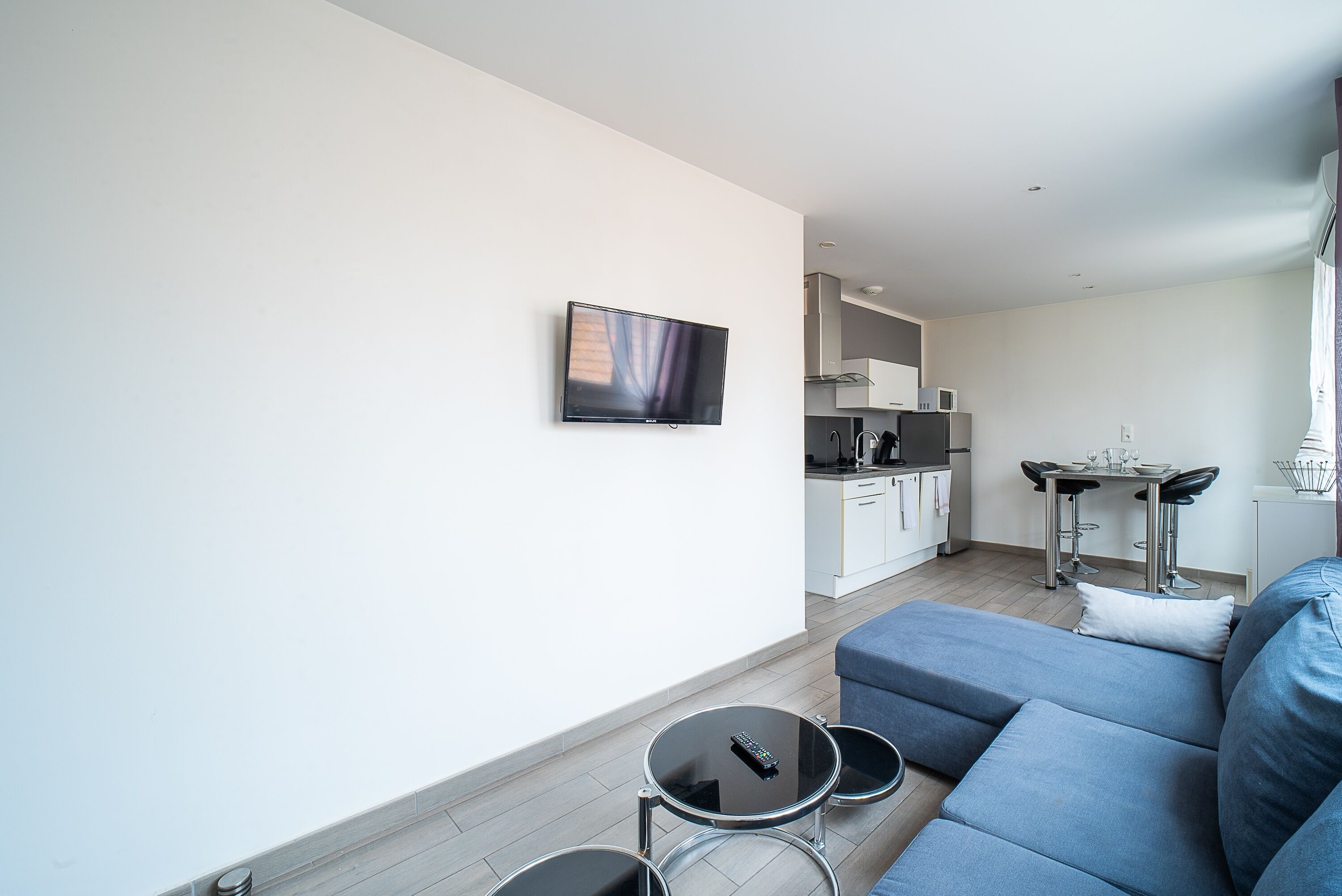 Un salon moderne avec un canapé bleu, une petite table basse ronde et un téléviseur à écran plat fixé au mur.
