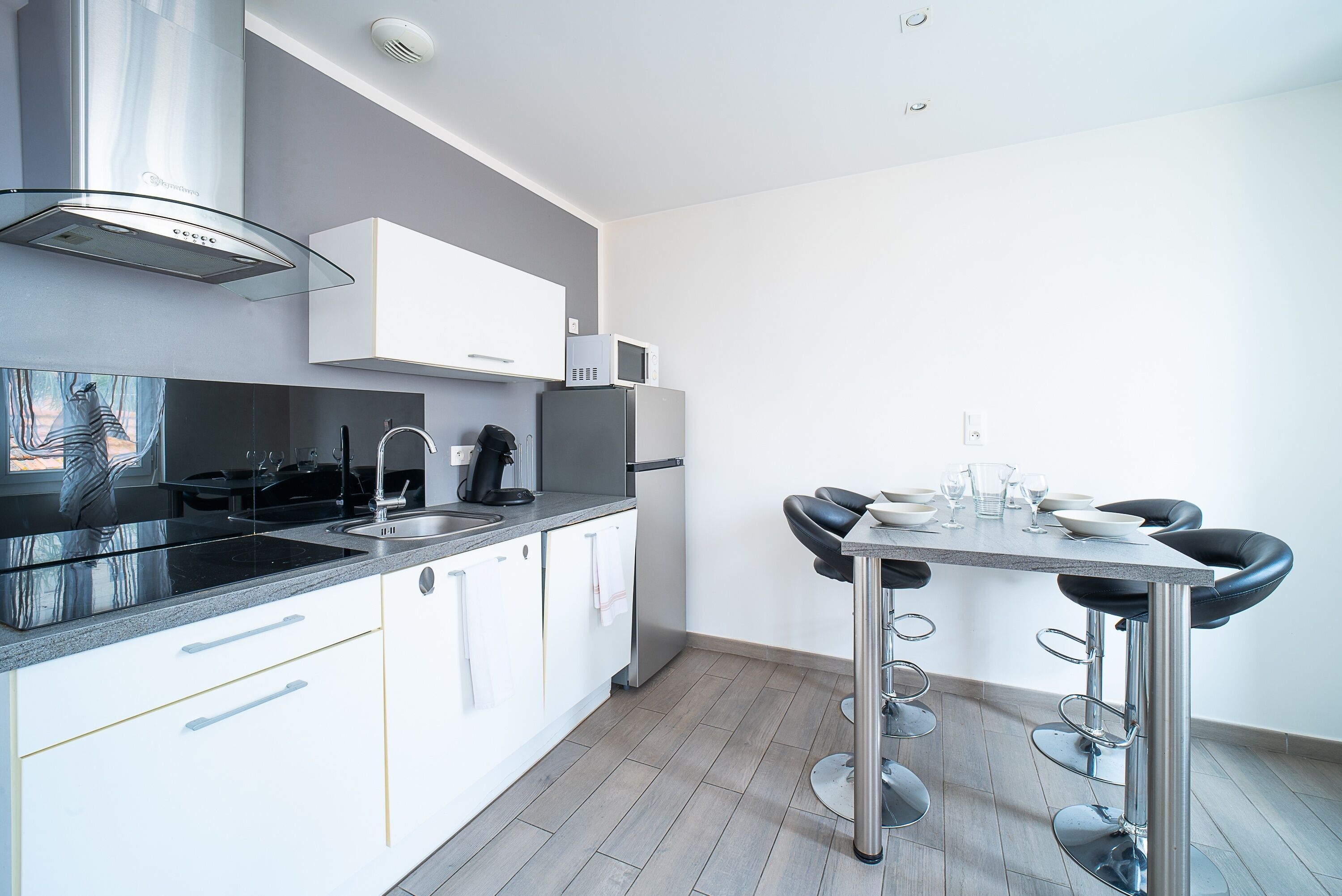 Une cuisine moderne avec des armoires blanches, une hotte de cuisinière en acier inoxydable, un four à micro-ondes et un coin repas comprenant une table et des tabourets de bar.