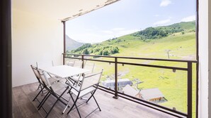 Un balcón con mesa y sillas, con vistas a un paisaje verde con colinas y cielo despejado.