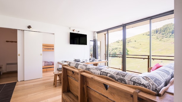 Una habitación moderna con un ventanal grande, un banco de madera, una cama y un televisor de pantalla plana.