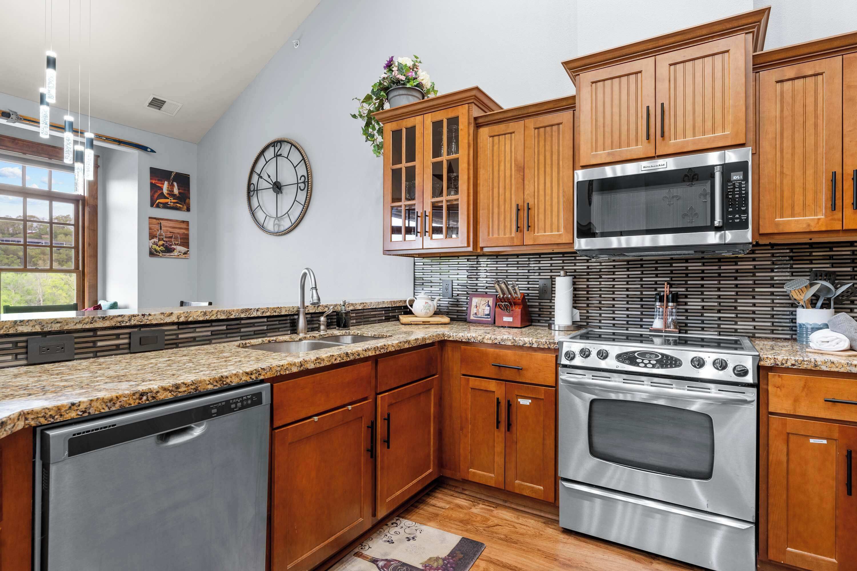 A modern kitchen with wooden cabinets, stainless steel appliances, granite countertops, and a clock on the wall.