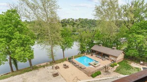 Une maison avec une piscine, entourée d’arbres et bordée d’un lac.