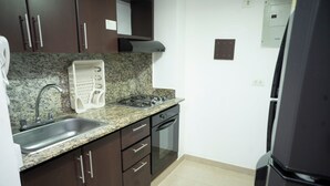 A kitchen with dark brown cabinets, a granite countertop, a stainless steel sink, a built-in oven, and a black refrigerator. -  2-bedroom apartment in Bocagrande- Cartagena (Bolívar)