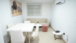 A dining area with a white table and chairs, a beige sofa, and a small pink ottoman. -  2-bedroom apartment in Bocagrande- Cartagena (Bolívar)