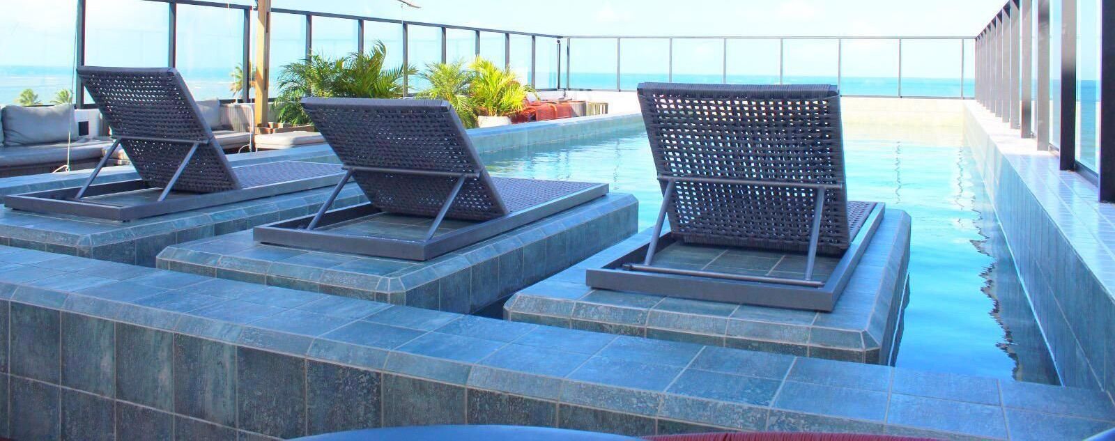 Un espace aménagé au bord de la piscine, avec des chaises longues et une vue sur l’océan.